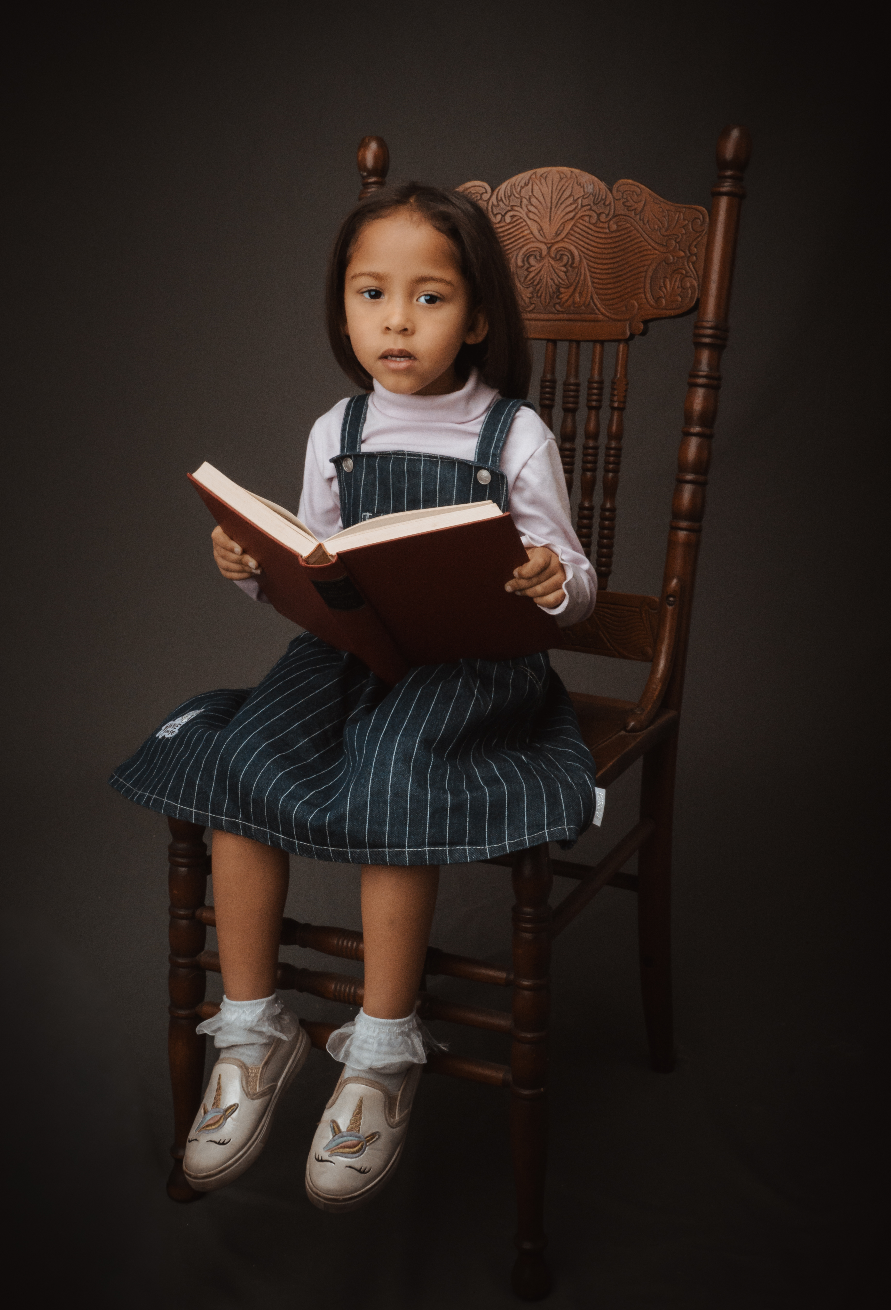 Young child seated in a wooden chair holding a book