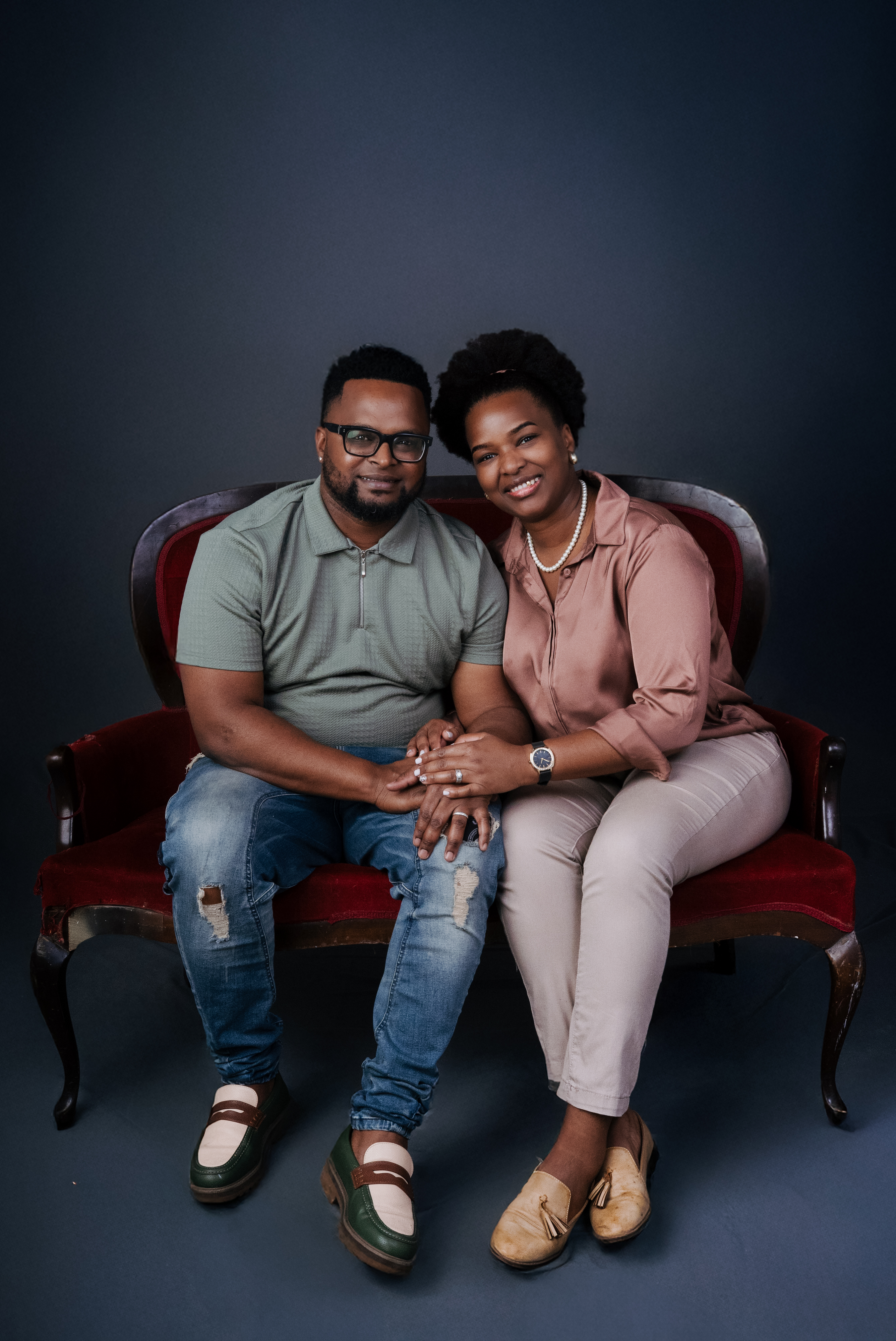 Couple seated together on a vintage red couch in the studio